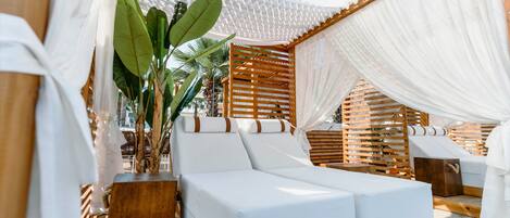 A sunlit outdoor lounge area with white cushioned seating and wooden structures.