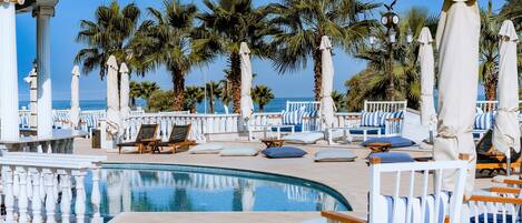 A poolside area with lounge chairs, umbrellas, and palm trees.