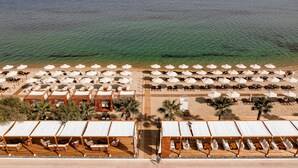 Vista aérea de um resort à beira-mar, com vários espreguiçadeiras, guarda-sóis e cabanas de madeira.