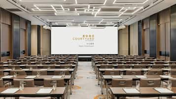 A conference room with rows of tables and chairs, a large screen at the front, and a modern ceiling design.