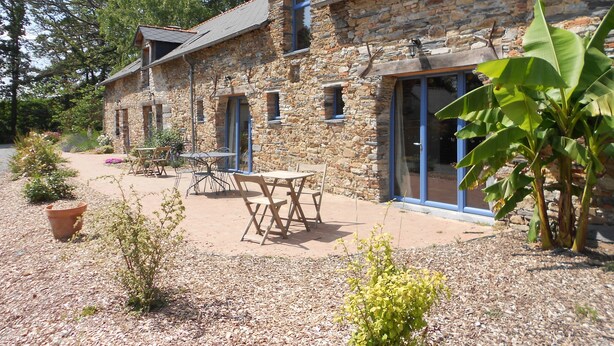 A stone building with a patio area, outdoor seating, and a large window. - Le Chêne Blanc (Plessé)