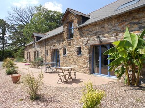 A stone building with a patio area, outdoor seating, and a large window. - Le Chêne Blanc (Plessé)