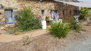 A stone building with a sloped roof, a small window, and a pathway leading to a white table and chairs. - Le Chêne Blanc (Plessé)