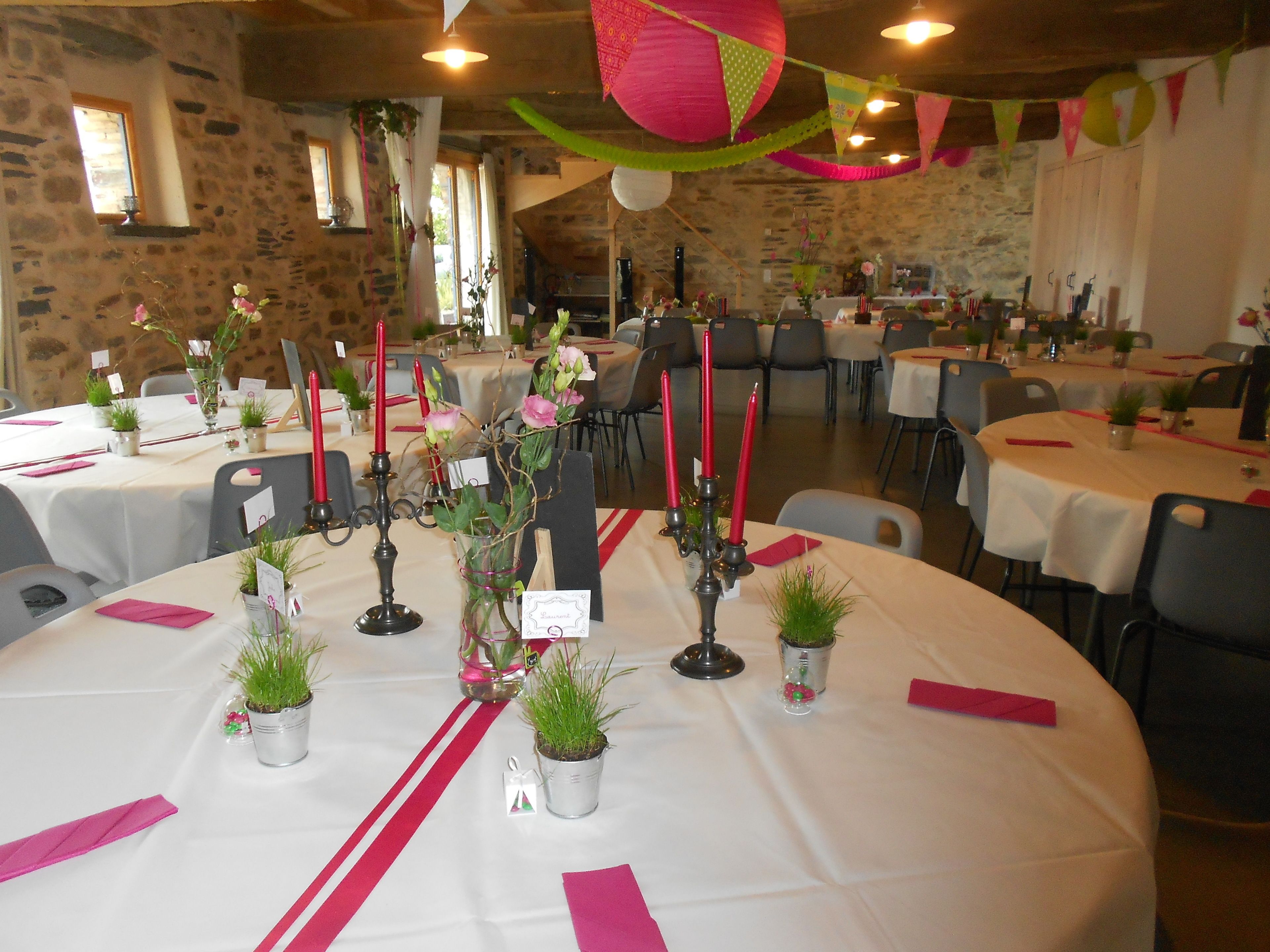 Une salle de banquet avec des tables rondes dressées pour un événement formel, agrémentée de nappes blanches, de serviettes rouges et de petits plants en pot.