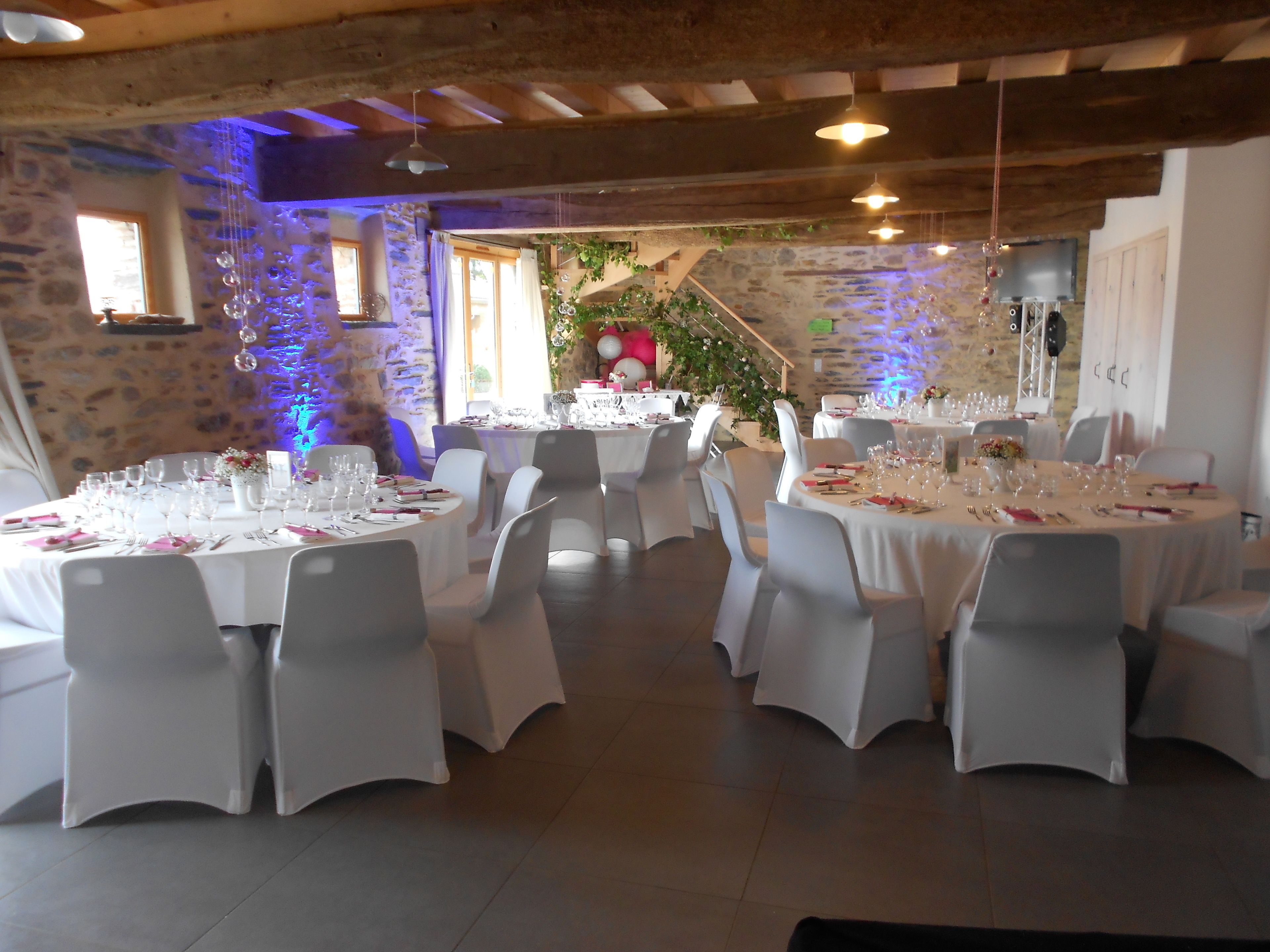 A restaurant with round tables set for dining, white chairs, and a rustic stone wall in the background.