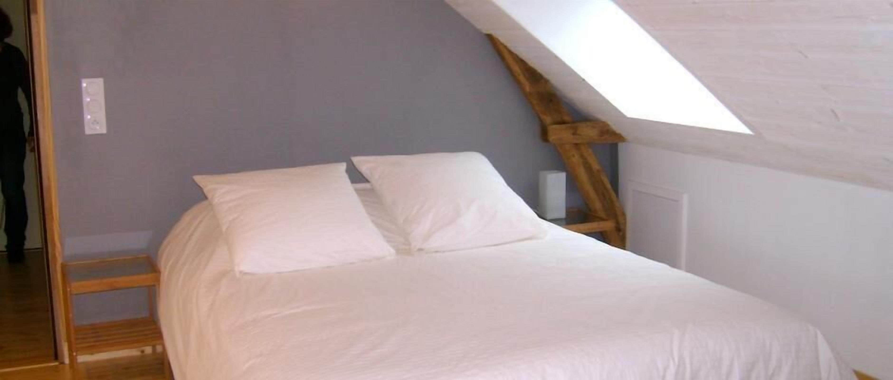 Une chambre avec un plafond en pente et un puits de lumière, comprenant un lit avec une literie blanche.