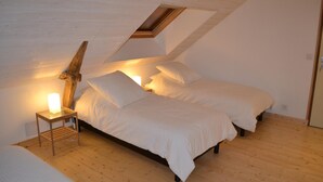 A bedroom with a sloped ceiling, a bed with white bedding, a bedside table with a lamp, and a wooden headboard. - Le Chêne Blanc (Plessé)