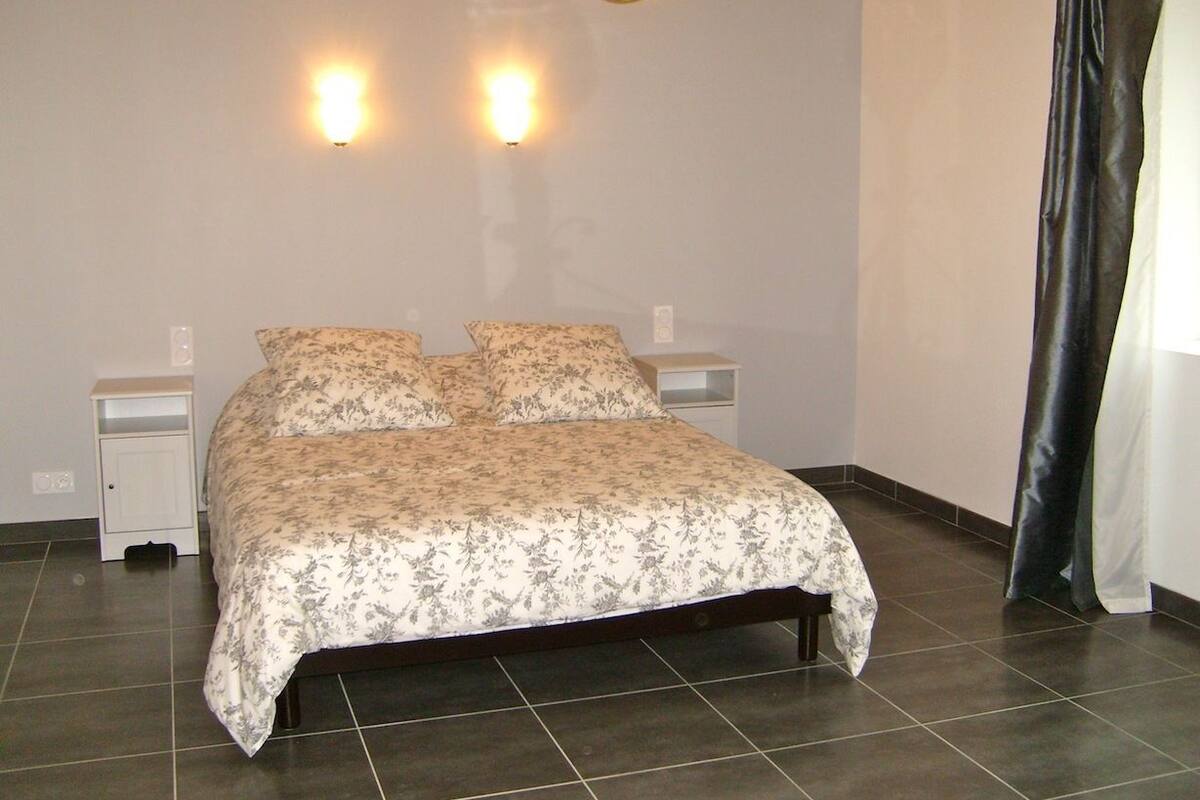 Quarto com cama, duas mesas de cabeceira e duas luzes na parede.