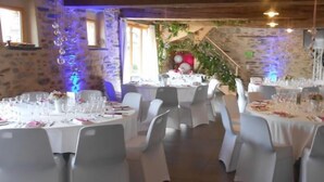 A dining area with round tables set for a meal, white chairs, and a rustic stone wall. - Le Chêne Blanc (Plessé)