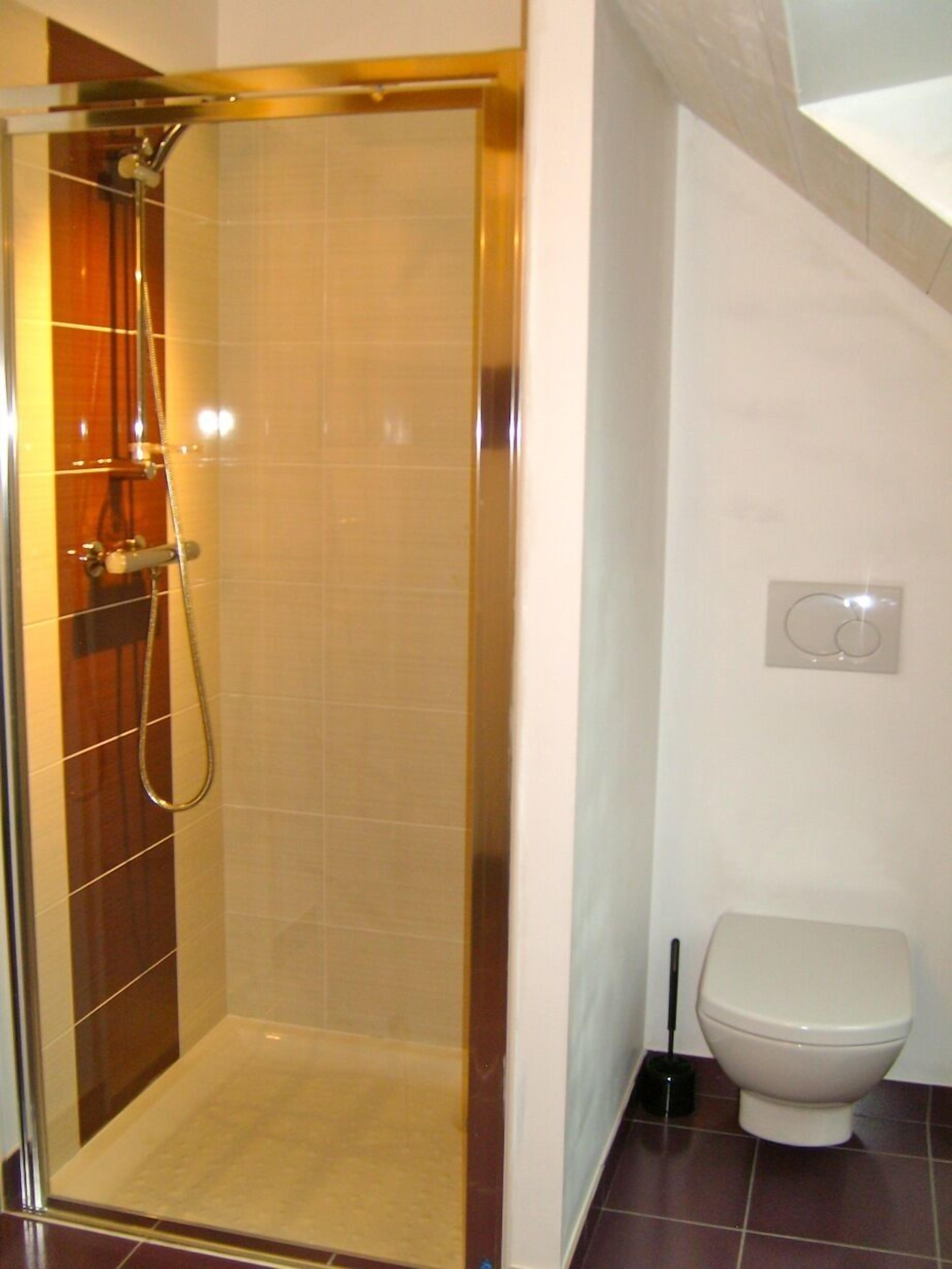 Un baño con ducha de mampara de vidrio, inodoro blanco y piso de baldosas.