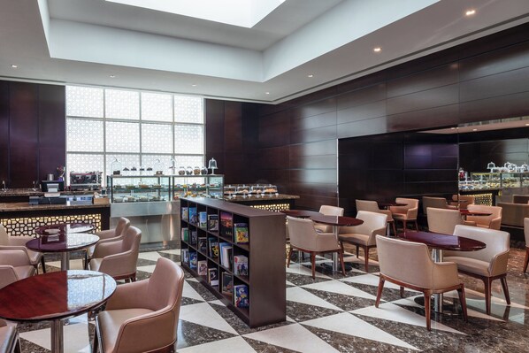 A modern hotel lobby with a checkered floor, a bar area with a wine cooler, and a seating area with bookshelves. - Four Points by Sheraton Sharjah (Sharjah)