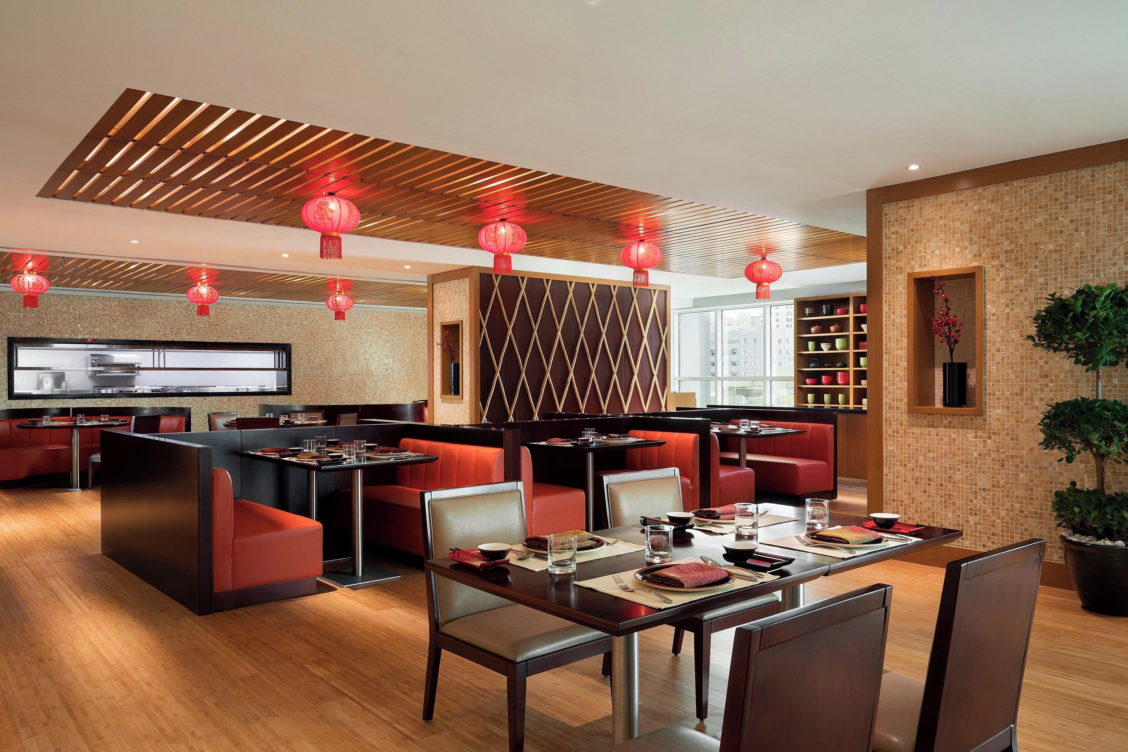 A modern restaurant with wooden ceiling panels, red lanterns, and a central island with seating.