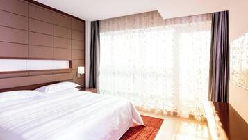 Een hotelkamer met een groot bed, een houten hoofdeinde, een nachtkastje en een groot raam met gordijnen.