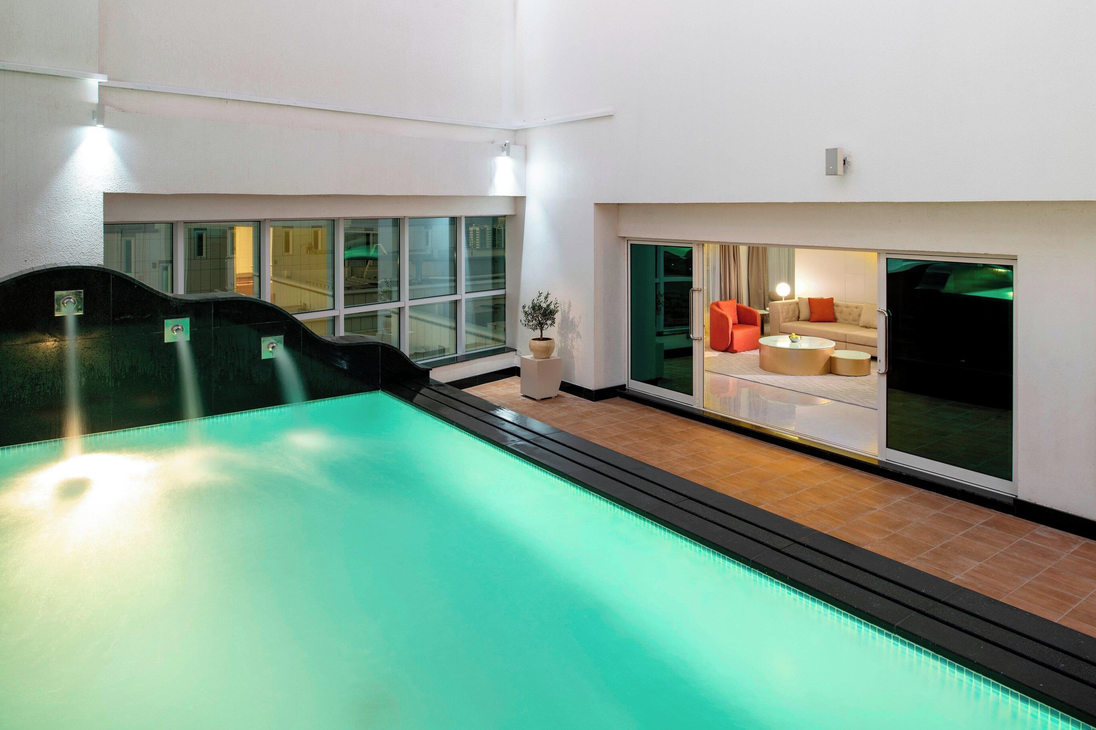 Une piscine intérieure au design moderne, un espace détente avec un canapé et des fauteuils, et de grandes fenêtres laissant entrer la lumière naturelle.