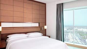 A hotel room with a large bed, a wooden headboard, a nightstand, a lamp, and a large window with a view of a cityscape.
