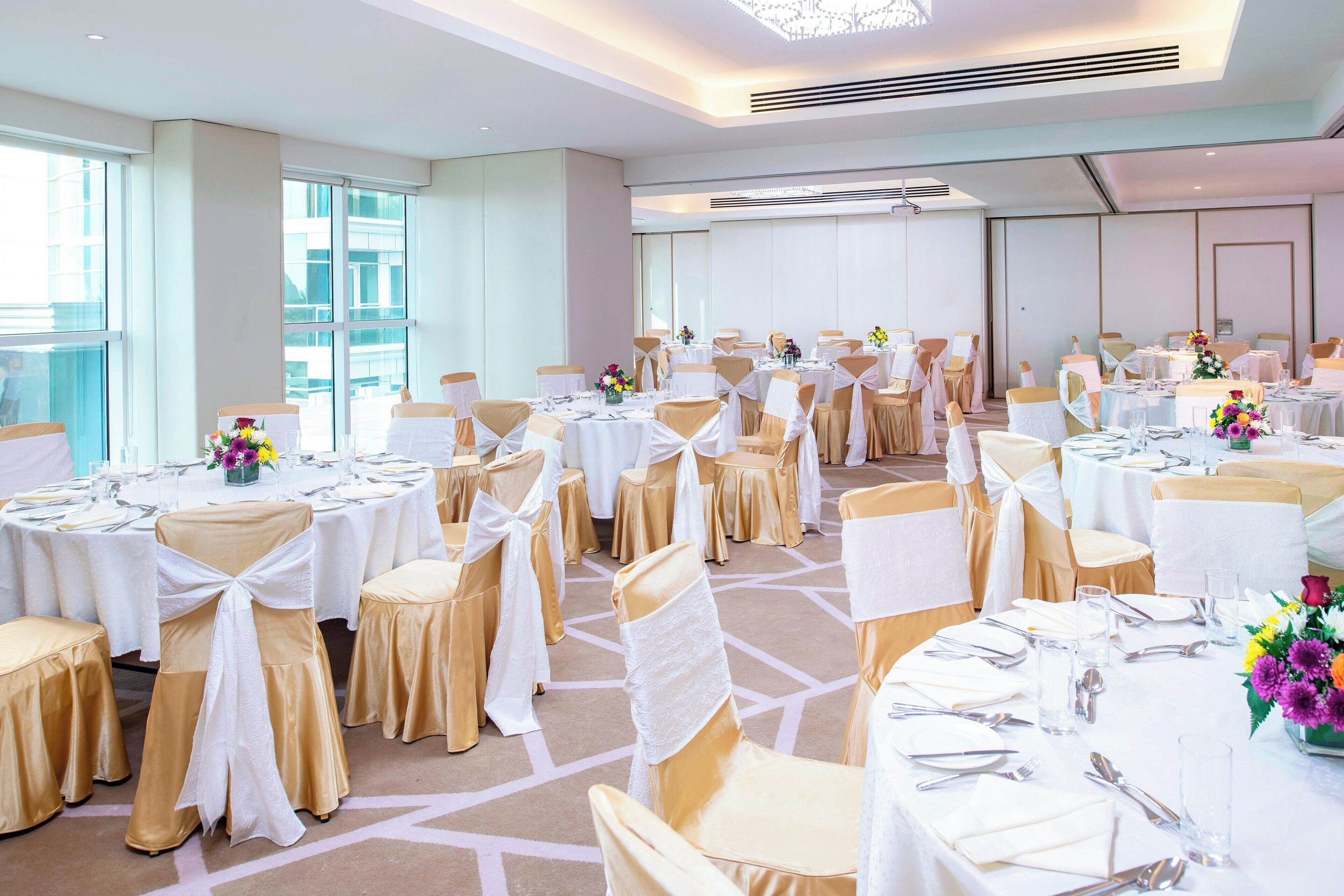 A banquet hall with round tables, chairs with white and gold sashes, and floral centerpieces.
