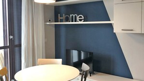 Ein modernes Wohnzimmer mit einem runden Esstisch, zwei Stühlen, einem Flachbildfernseher und einem Schild mit der Aufschrift 'Home' an der Wand.