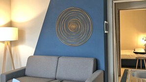 Ein modernes Wohnzimmer mit grauem Sofa, blauer Akzentwand und einem geometrischen Wandbild.