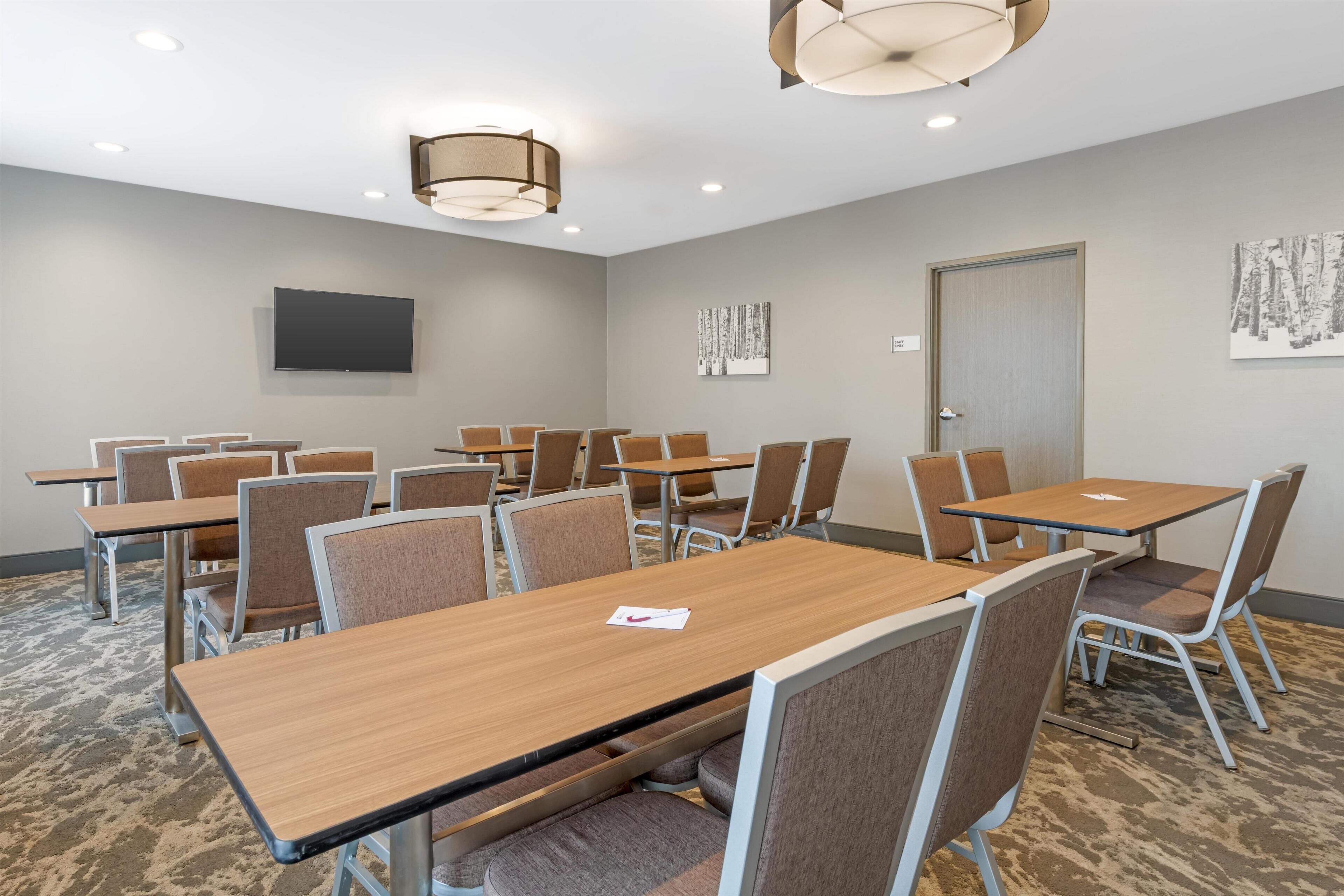 A conference room with multiple tables and chairs, a flat-screen TV mounted on the wall, and artwork on the walls.