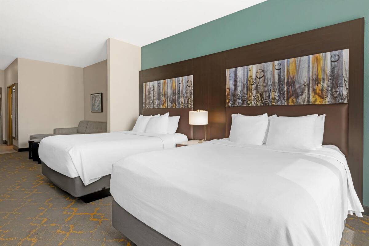 A hotel room with two beds, a sofa, a desk, and abstract artwork on the walls.