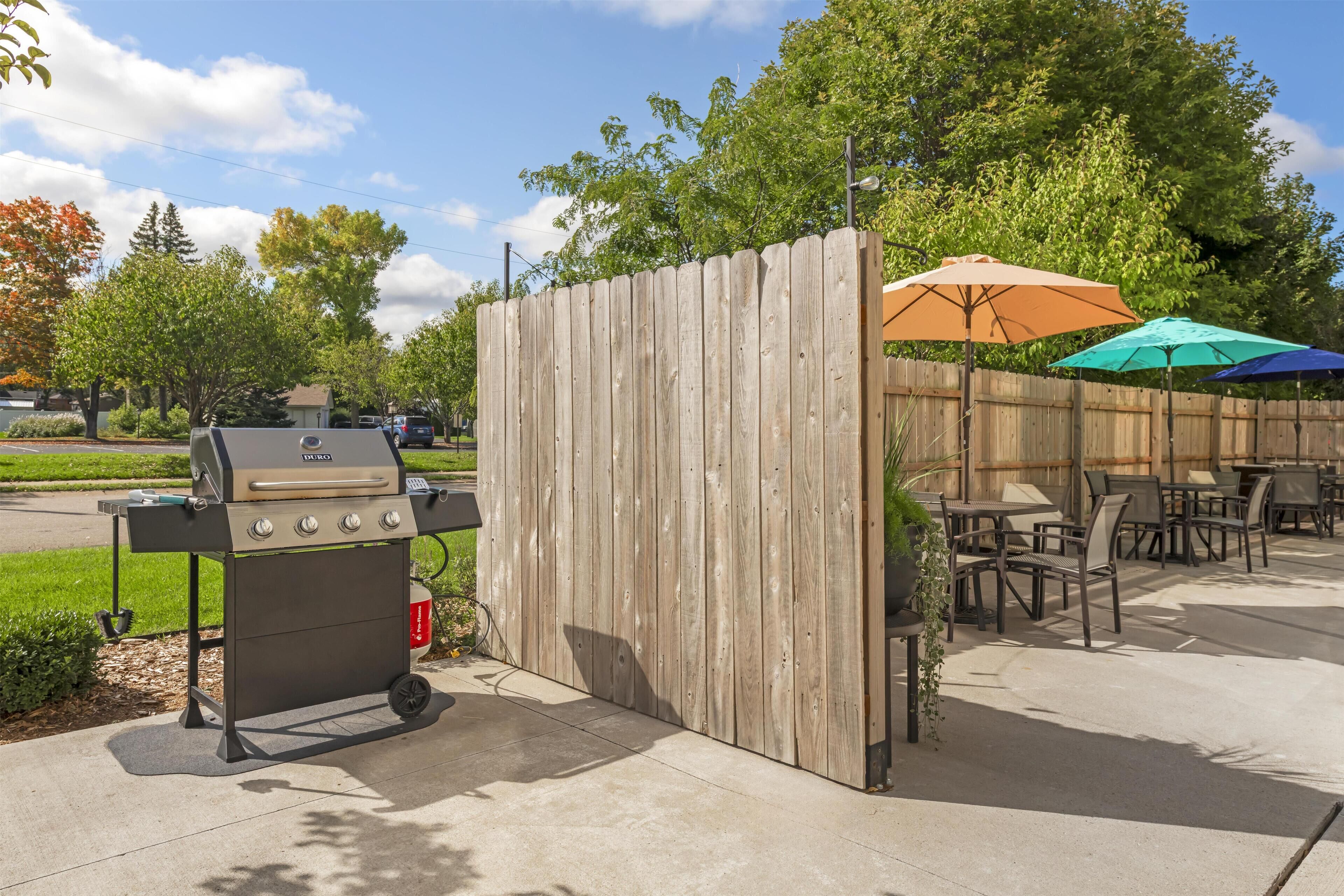 A patio area with a grill, outdoor seating, and umbrellas.