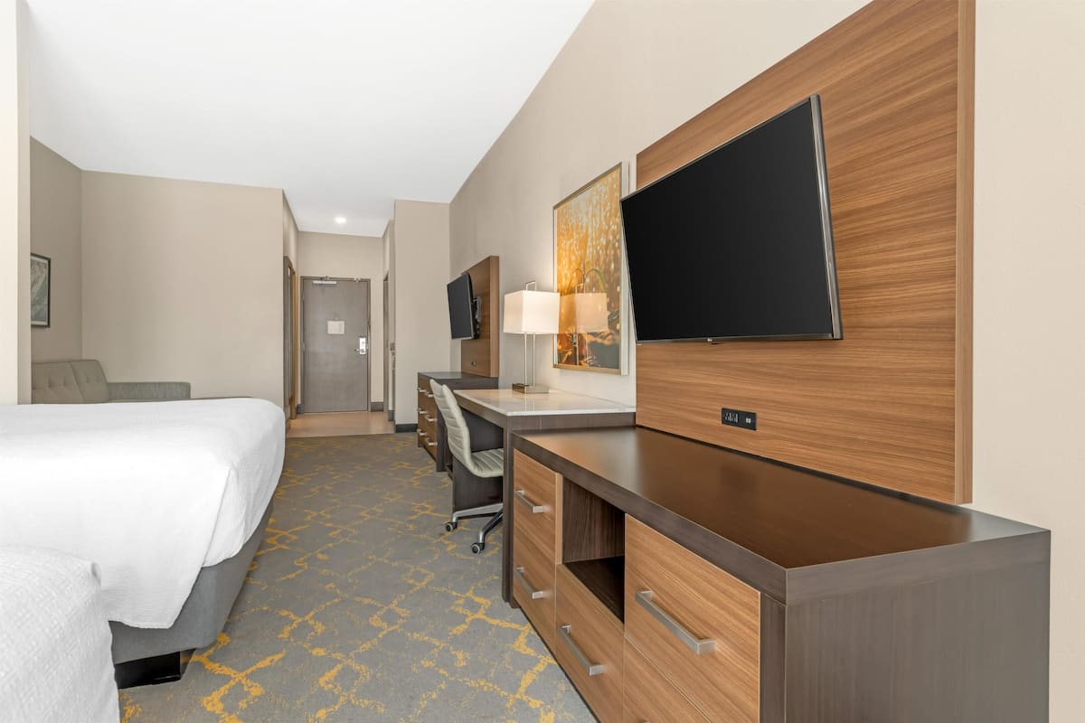 A hotel room with a bed, desk, chair, TV, and a lamp.