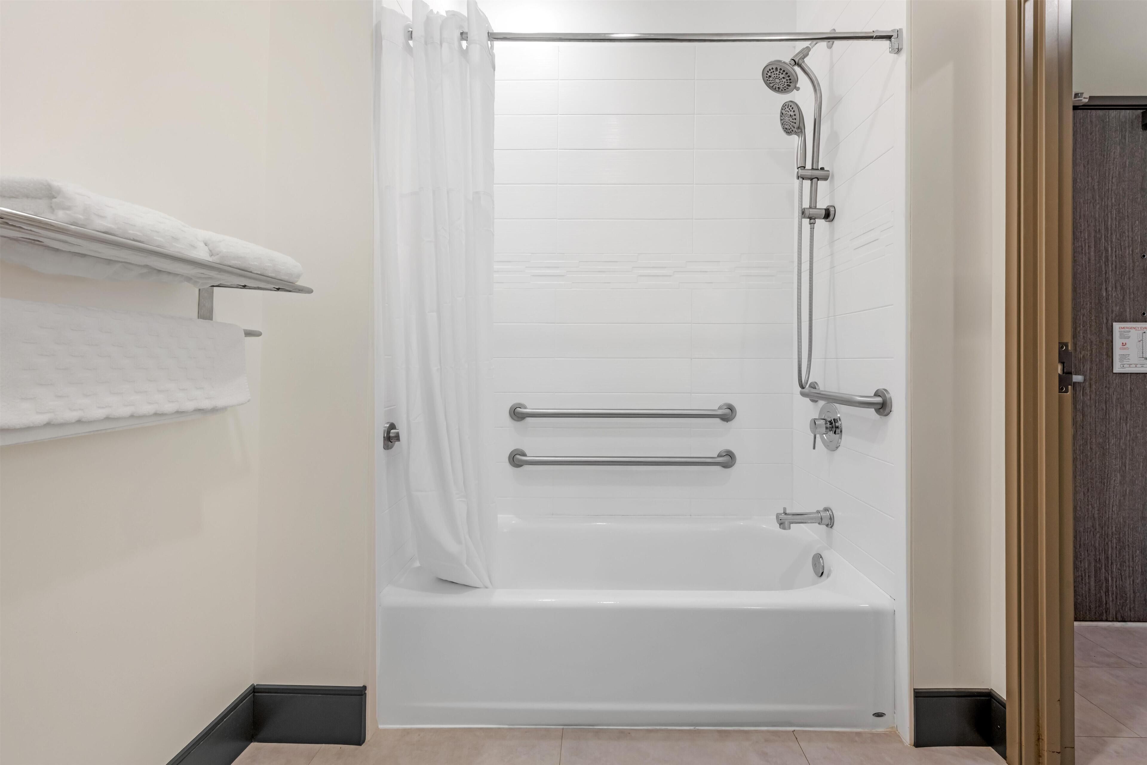 Une salle de bain moderne avec une douche à l’italienne, des barres d’appui et un mur recouvert de carreaux blancs.