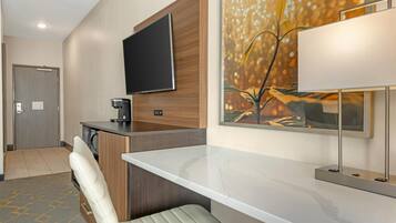 Habitación de hotel moderna con encimera de mármol, televisor de pantalla plana en la pared, cafetera y una obra de arte enmarcada.