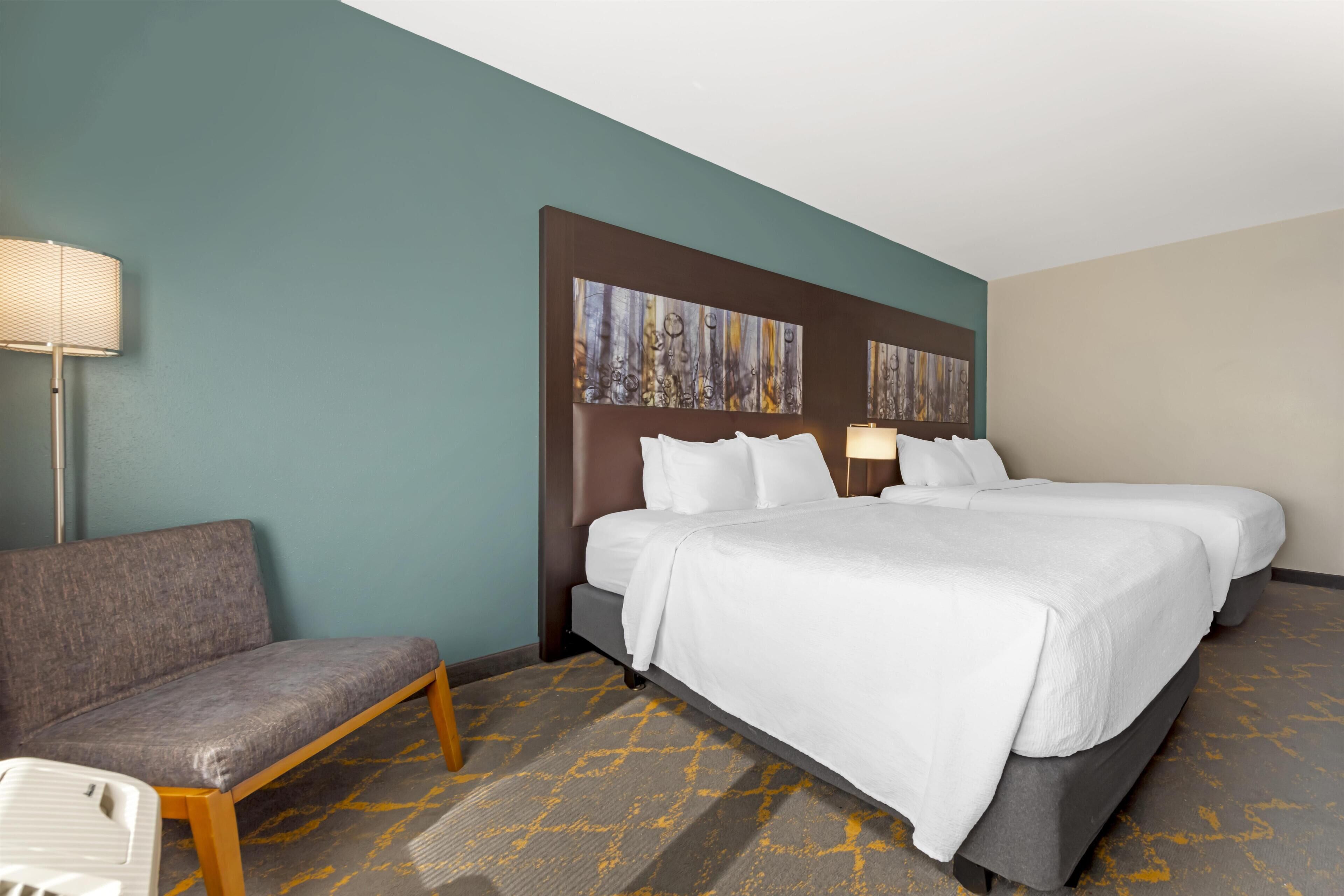 A hotel room with two beds, a sofa, a lamp, and abstract wall art.