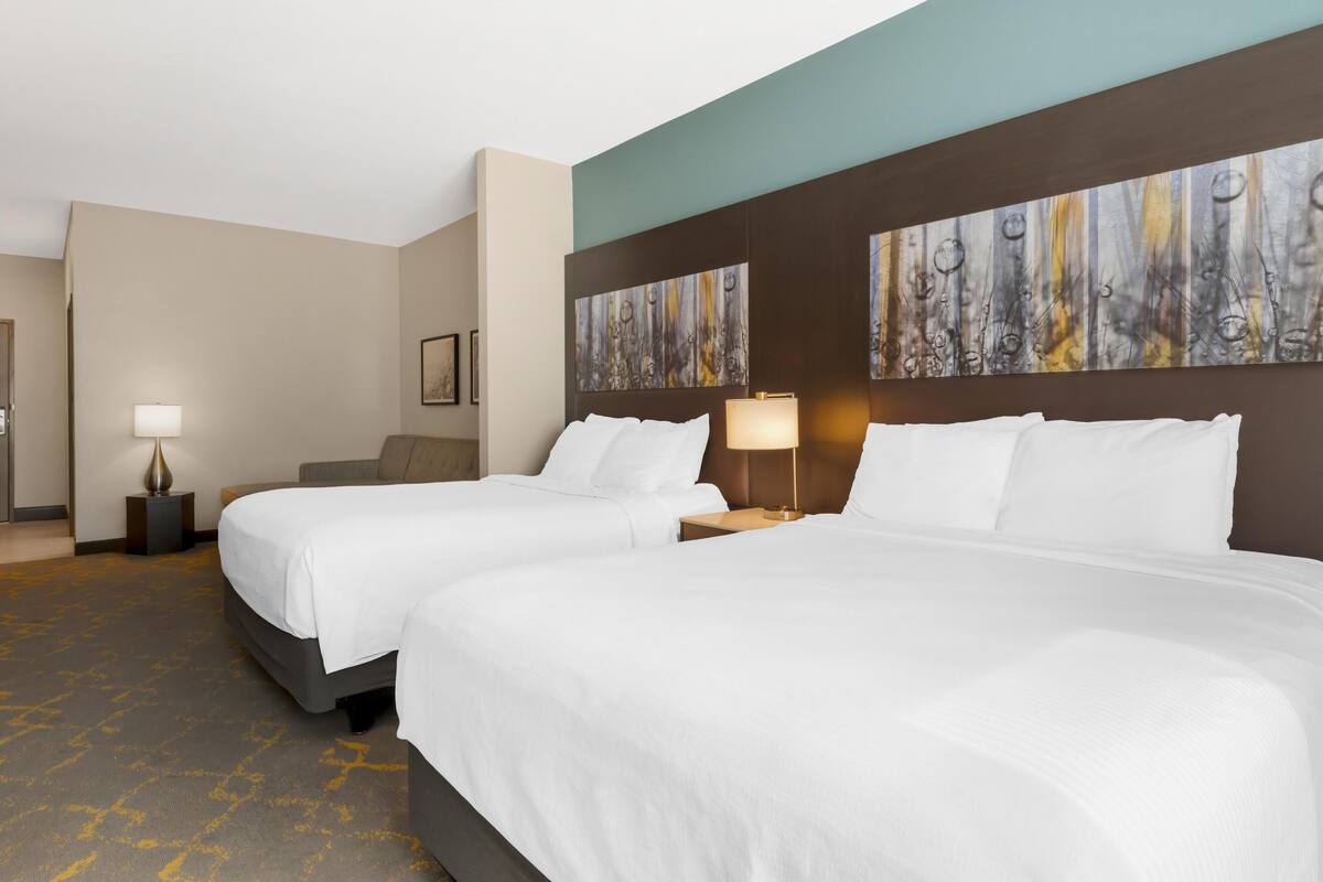 A hotel room with two beds, a large abstract painting on the headboard, and a carpeted floor.