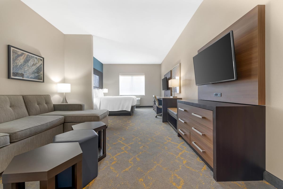 A hotel room with a sofa, a bed, a desk, a TV, and a lamp.
