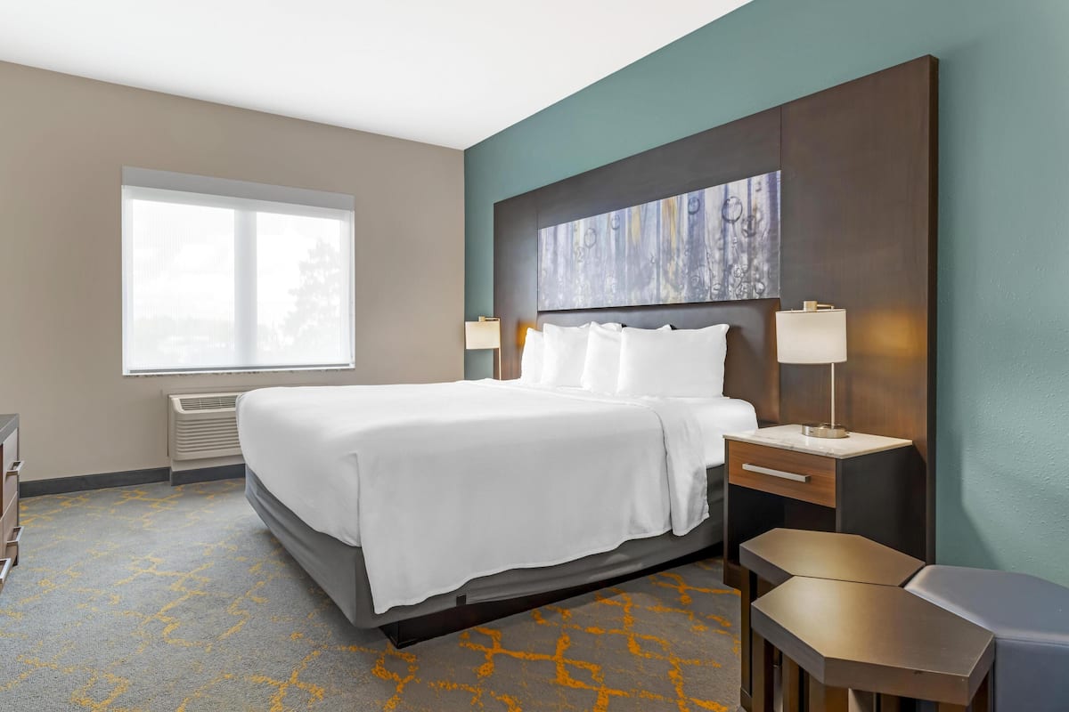A hotel room with a large bed, a desk, a chair, a window, and a painting on the wall.