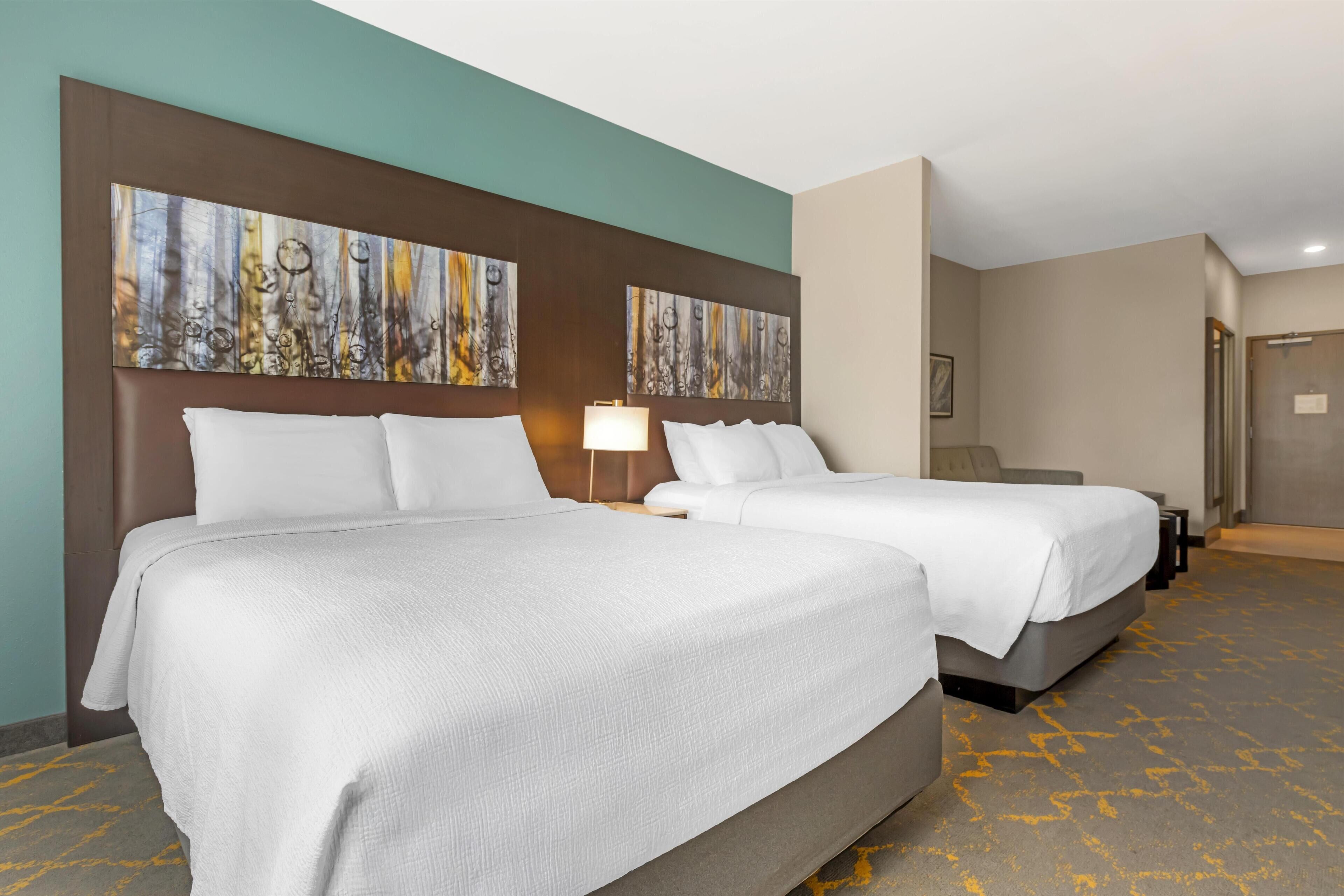 Ein Hotelzimmer mit zwei Betten, einem großen abstrakten Gemälde an der Wand und einem Teppichboden.