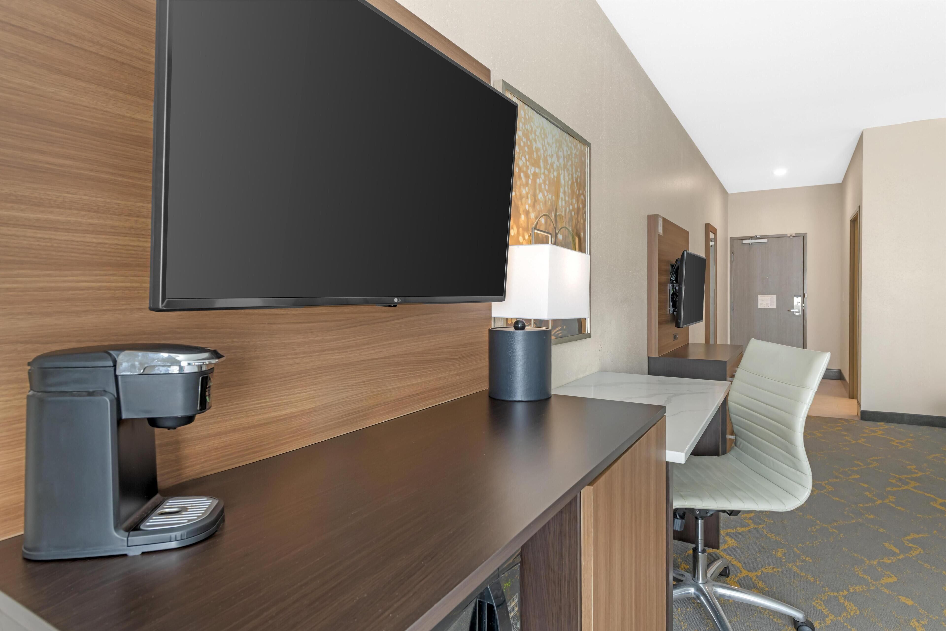 Une chambre d’hôtel équipée d’un téléviseur à écran plat, d’une machine à café, d’un bureau avec une chaise et d’une lampe.