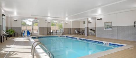 Une piscine avec une terrasse carrelée, une horloge et un espace détente comprenant des tables et des chaises.