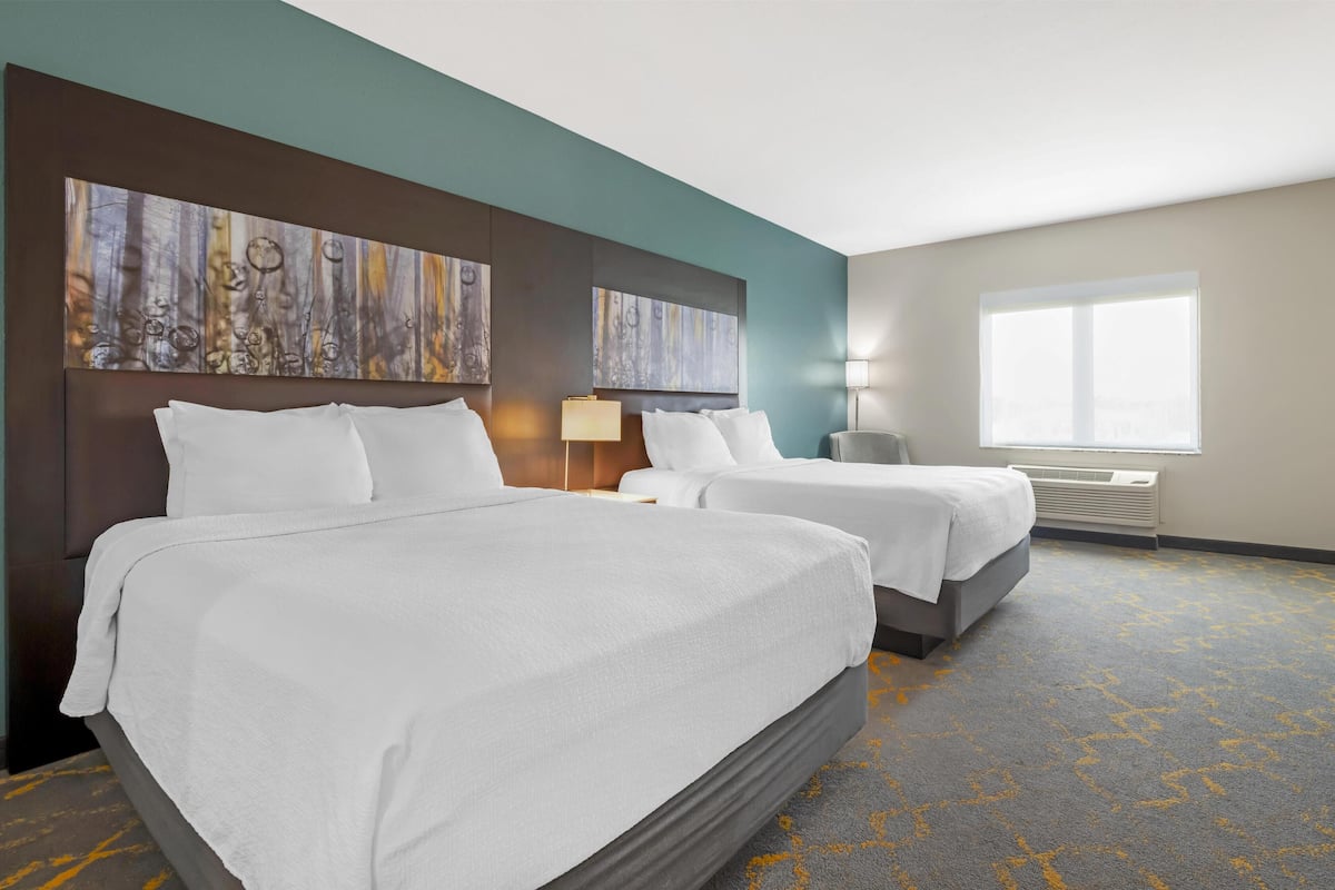 A hotel room with two beds, a large window, and artwork on the walls.