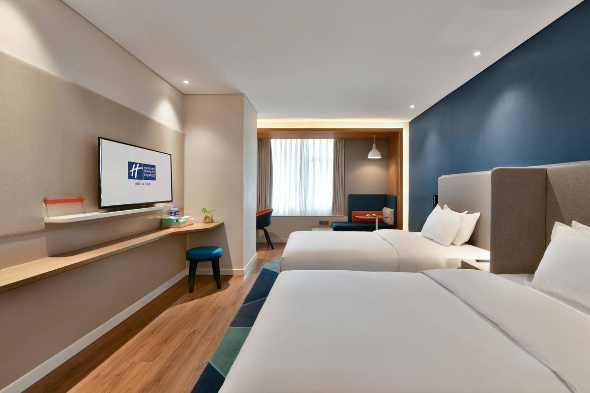 Una habitación de hotel con dos camas, un escritorio, un televisor y una ventana con cortinas.