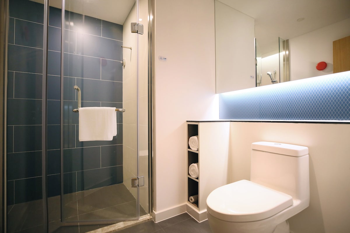 Un baño moderno con cabina de ducha de vidrio, inodoro blanco y estante empotrado con toallas.