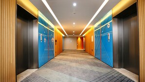 Un vestíbulo de ascensor moderno con alfombra estampada, paneles de madera y diseños geométricos azules en la pared.