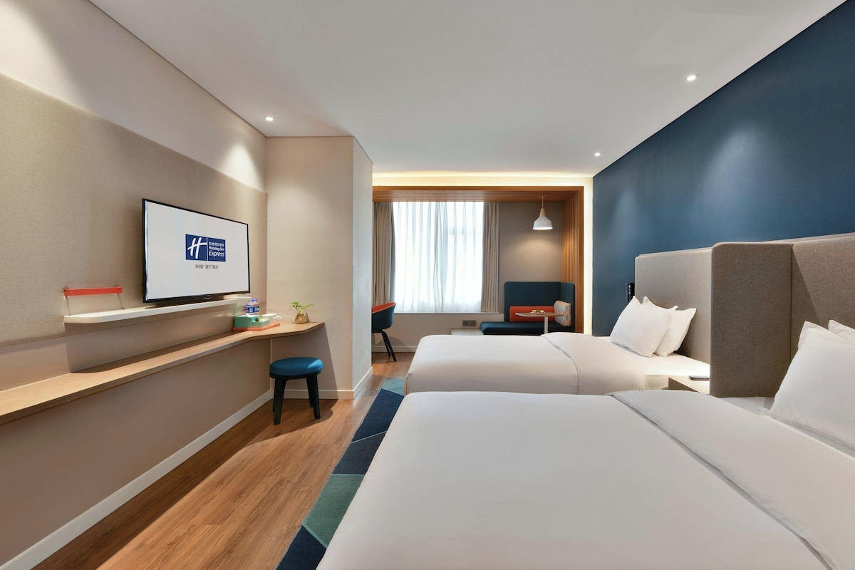 Una habitación de hotel con dos camas, un escritorio, un televisor y una ventana con cortinas.