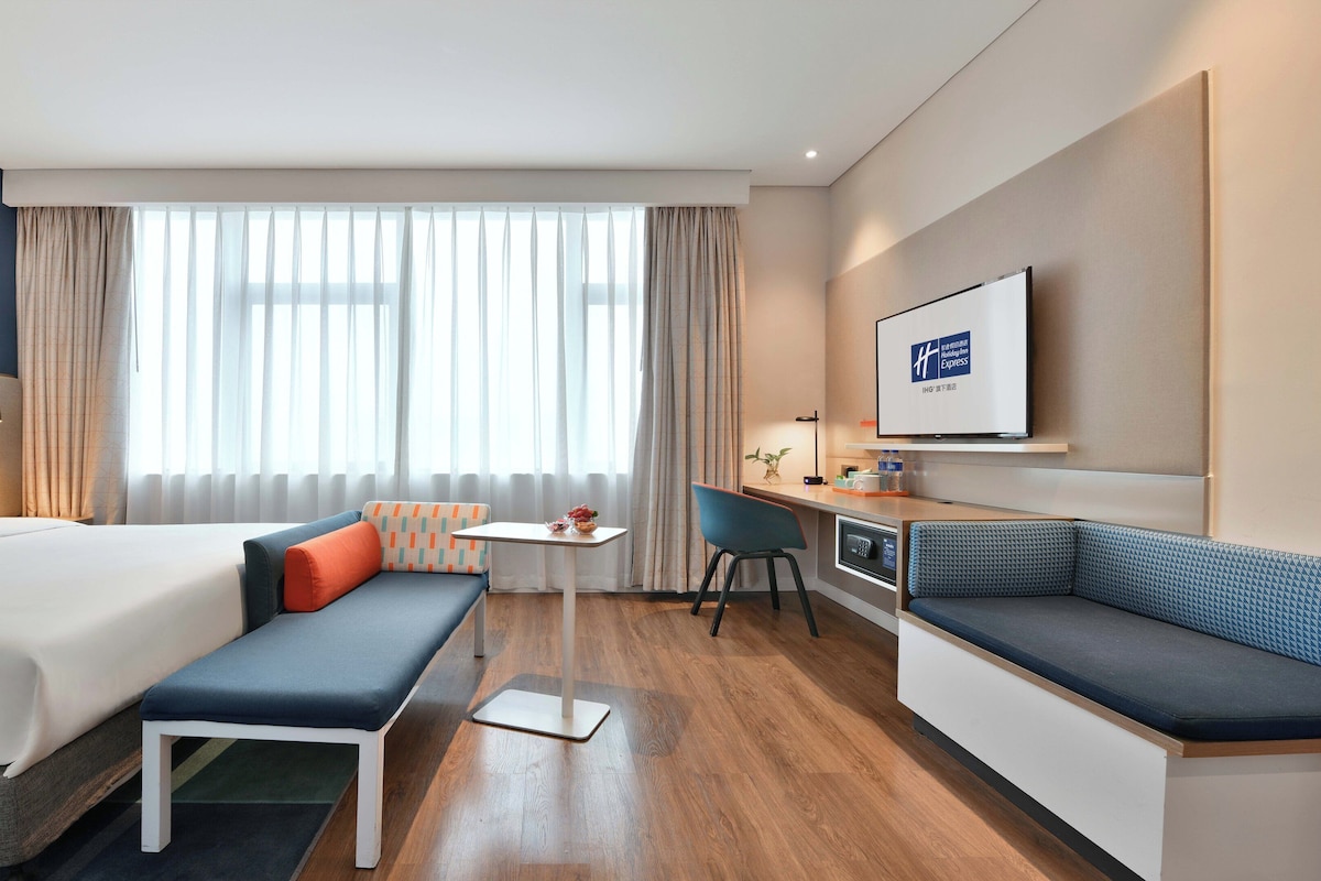 Una habitación de hotel con cama, escritorio, silla, sofá y televisión.