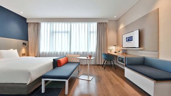Habitació d'hotel amb un llit, una taula de treball, una cadira, un sofà i una televisió.