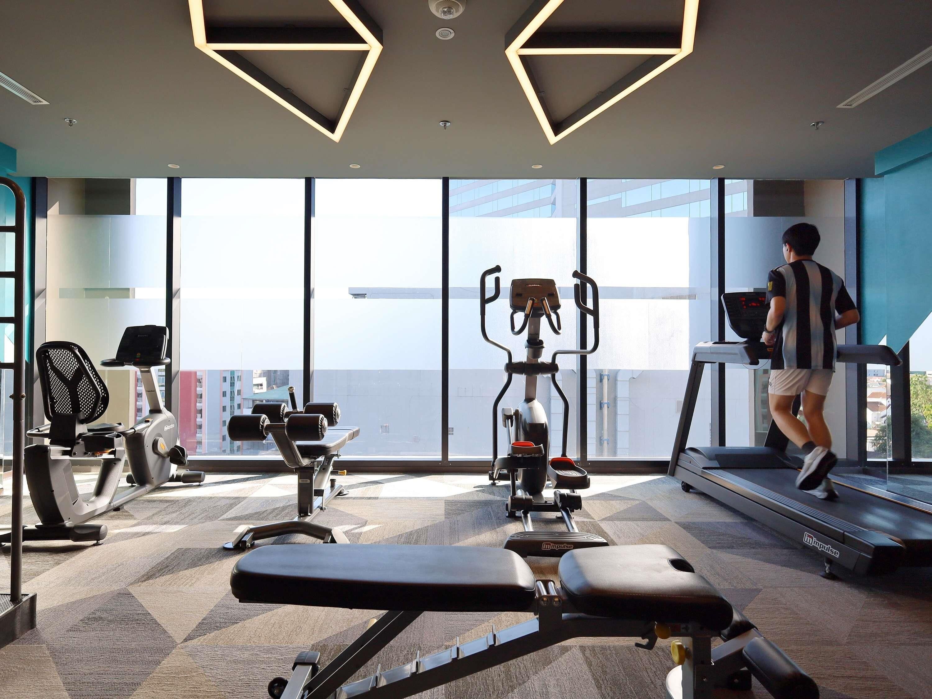 Une salle de sport équipée de matériel d’exercice, d’un tapis de course et de grandes fenêtres donnant sur la ville.