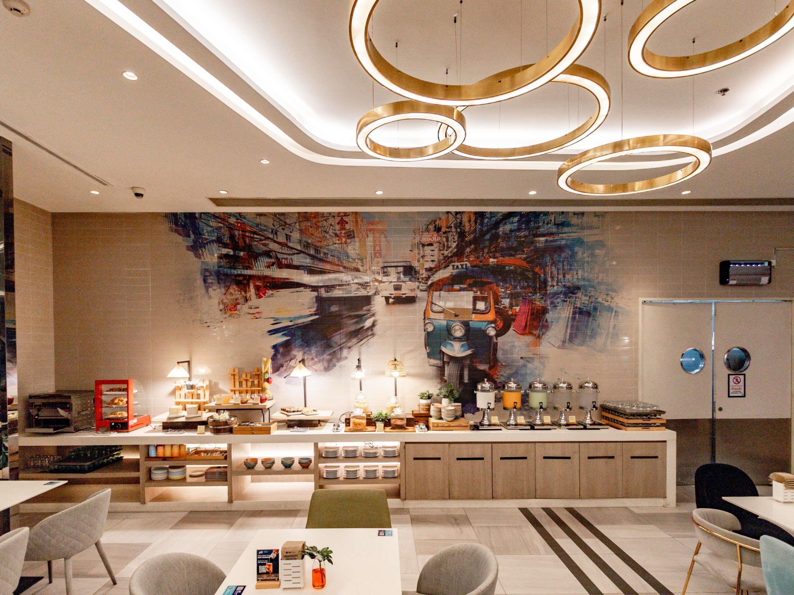 Un lobby moderno de hotel con una zona de bar central, arreglos de asientos y un gran mural abstracto en la pared.