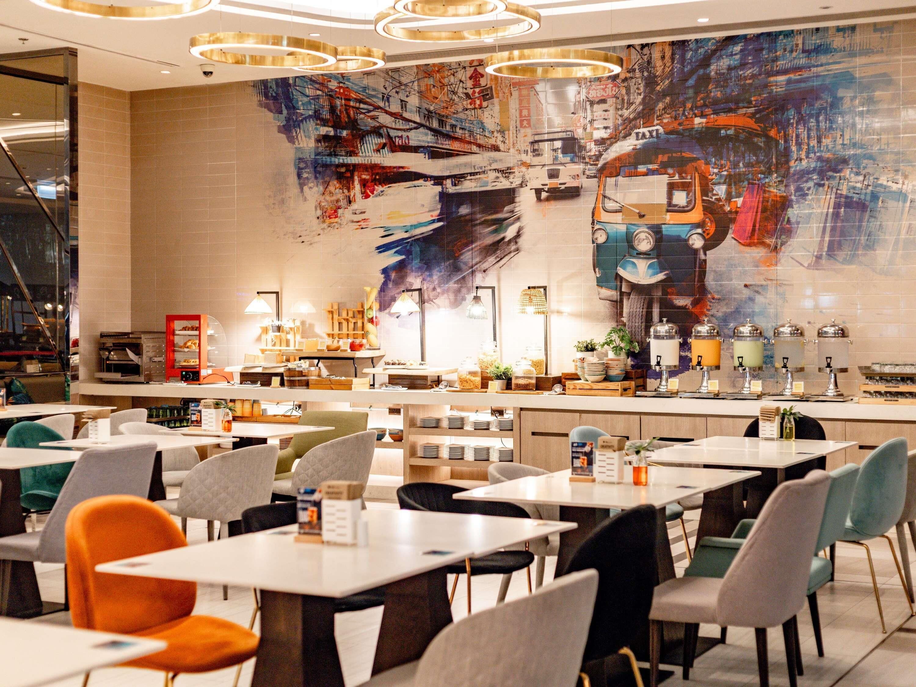 Un restaurante moderno con un mural grande, varias mesas para comer y diferentes opciones de asientos.