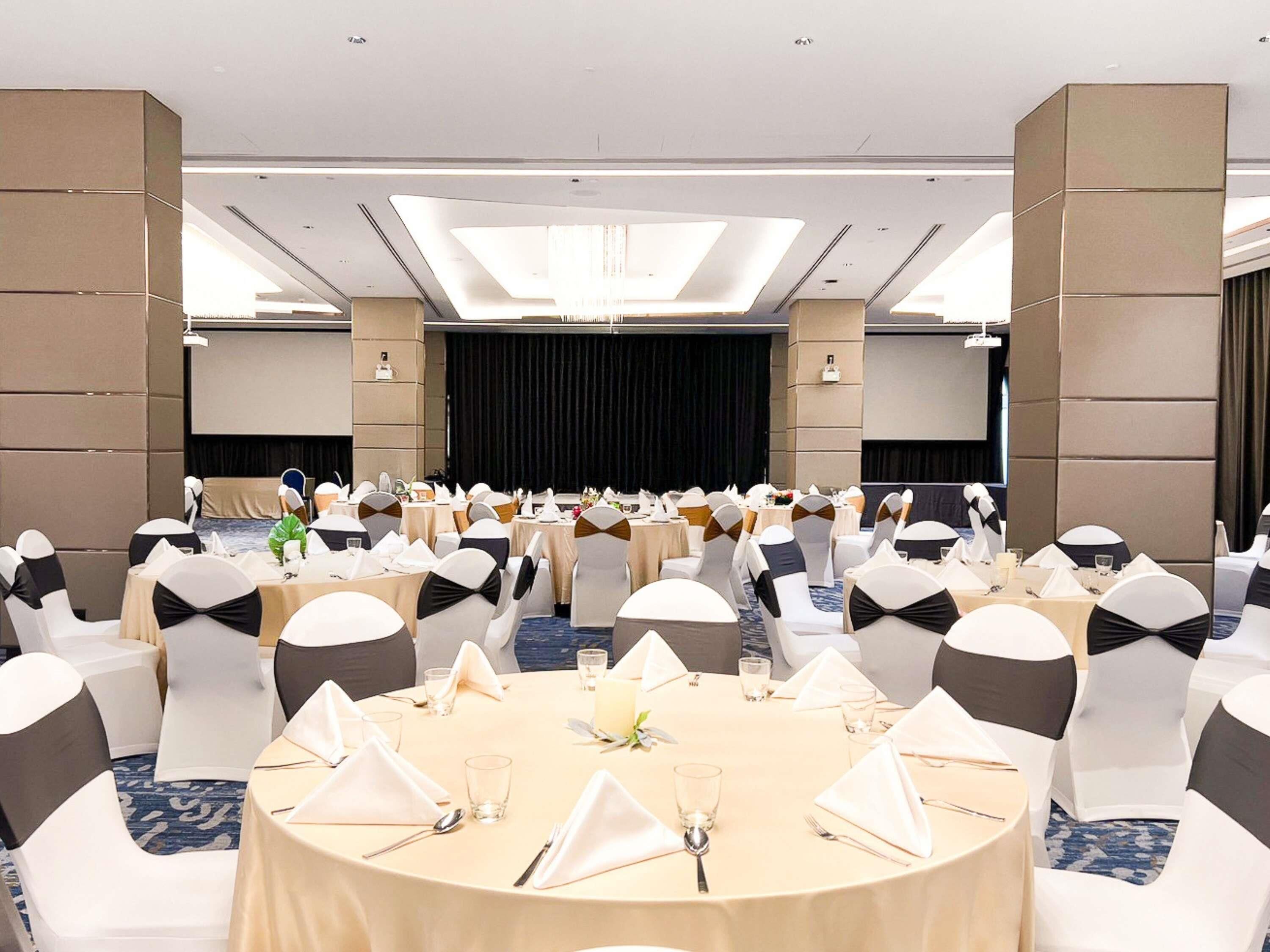 A banquet hall with round tables, white and black chairs, and a stage at the front.