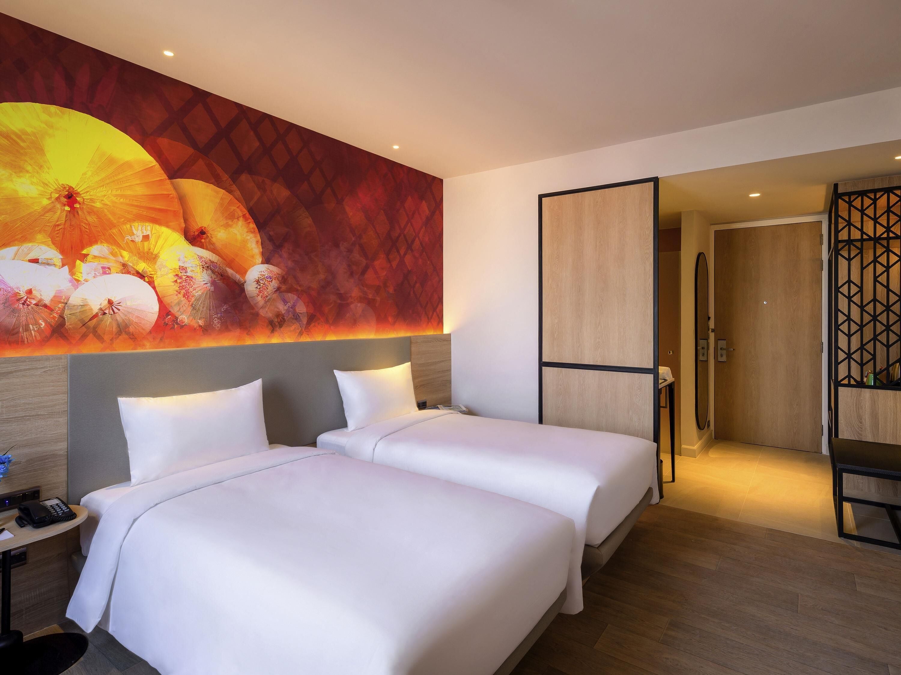 A hotel room with two beds, a large wall mural, a wooden floor, and a separate seating area.