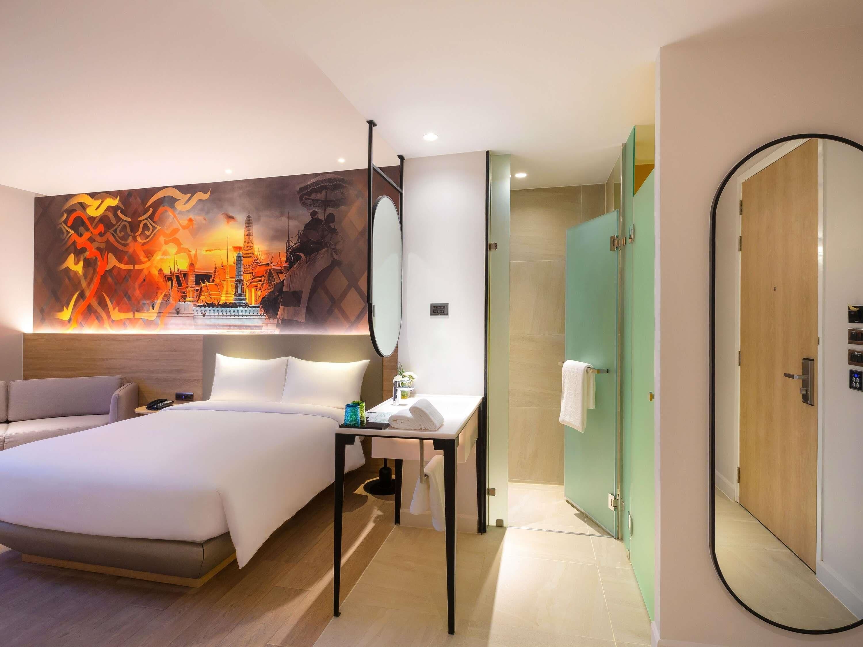 A hotel room with a bed, bedside table, mirror, and a wall with a large artwork.