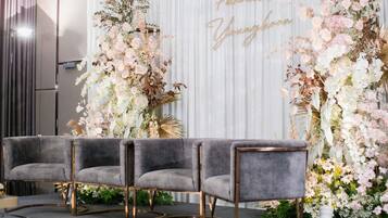 A room with a stage, three grey upholstered chairs with gold legs, and a backdrop with floral arrangements and the text 'Pannaros Youngoon'.