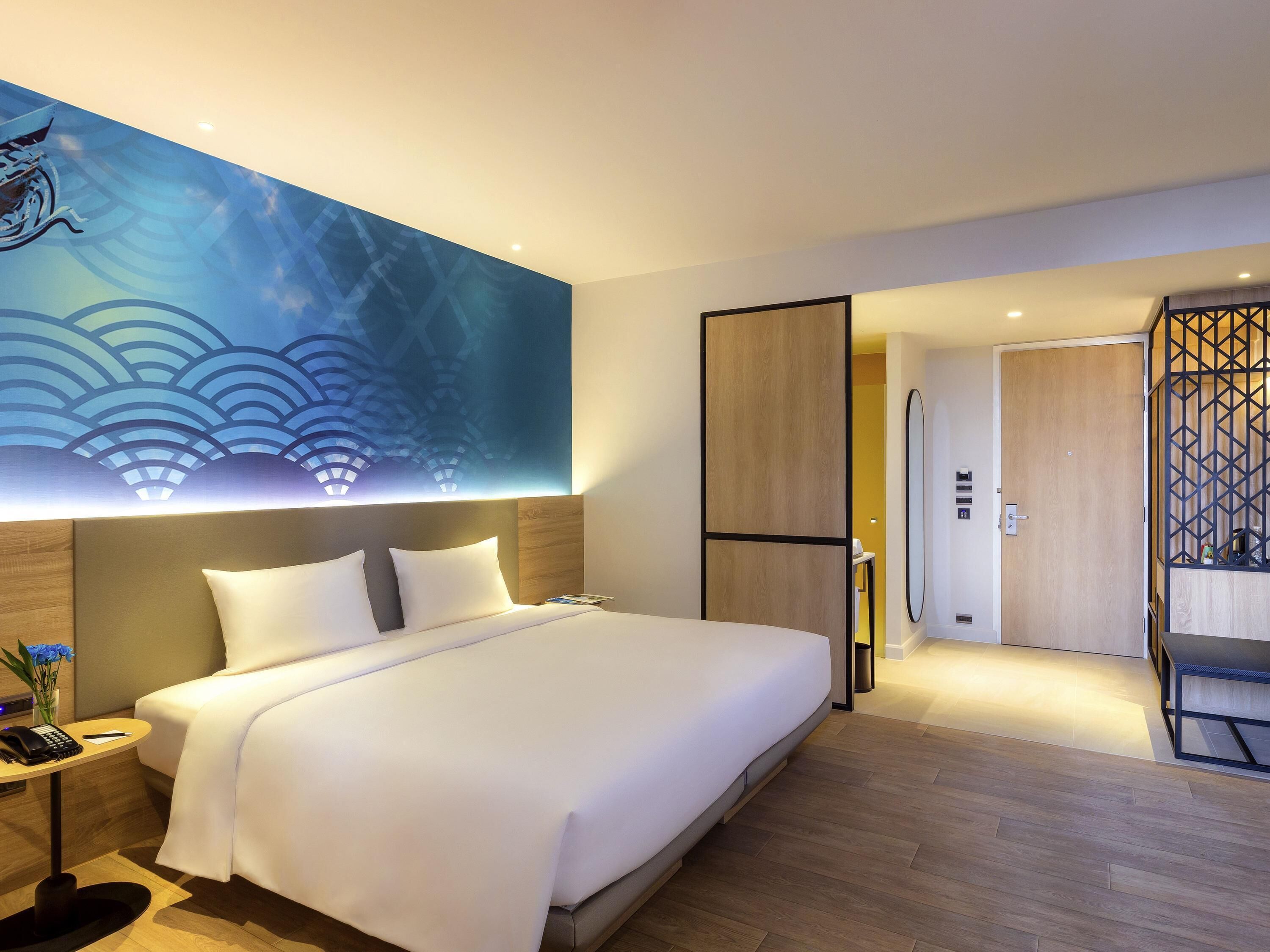 Una habitación de hotel moderna con una cama grande, una mesita de noche con teléfono y una obra de arte colgada en la pared.